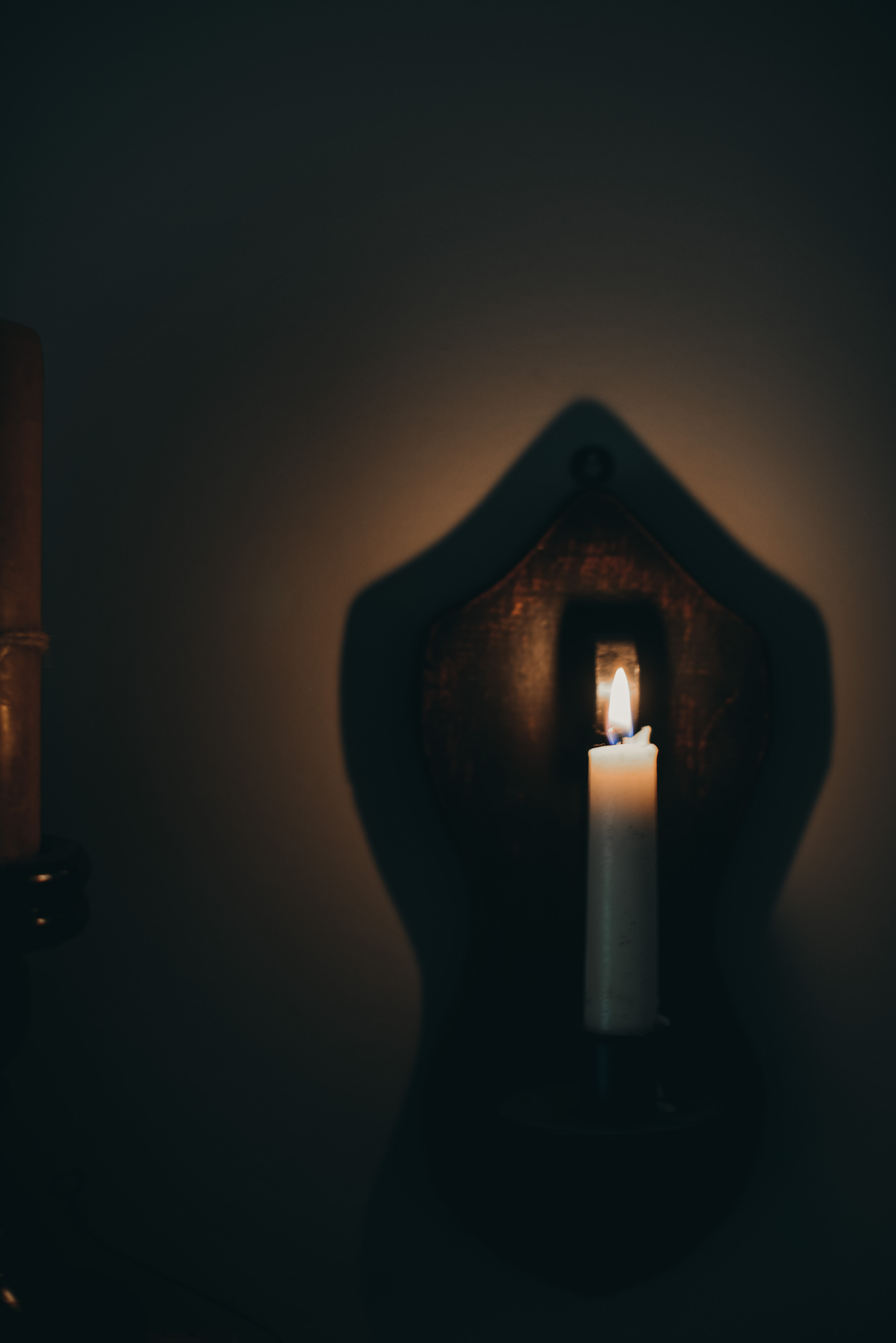 A white candle lit on a wooden holder, casting a unique shadow on the wall behind.